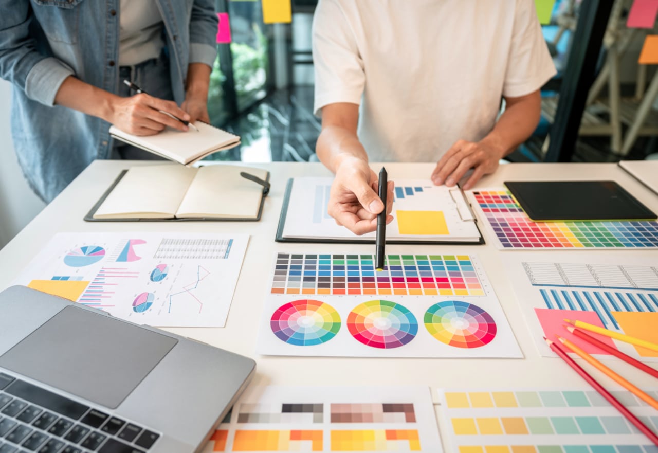 Equipo de diseño trabajando en la selección de paletas de colores y elementos visuales para un proyecto de branding, utilizando herramientas gráficas y un portátil